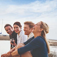A group of four friends posing by a lakeside, smiling and enjoying drinks, with a boat in the background.