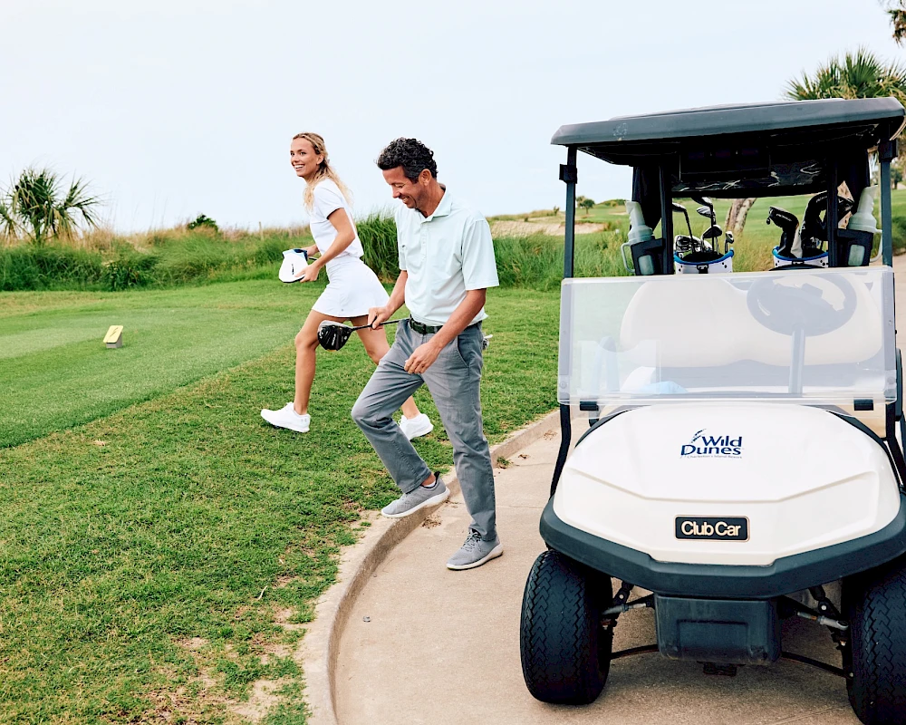 A couple playfully jog along a golf path beside a white golf cart on a sunny course, ready to hit their next shot.