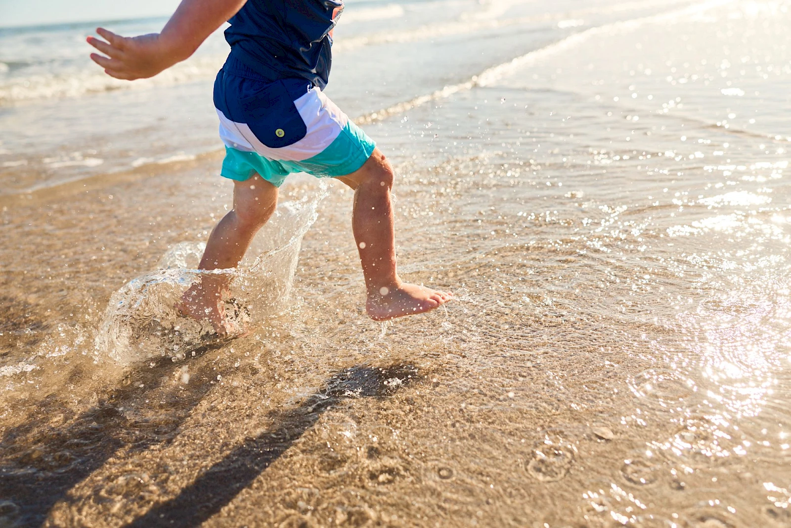 A child runs along the shore, splashing through shallow waves as water ripples with each step at the beach.