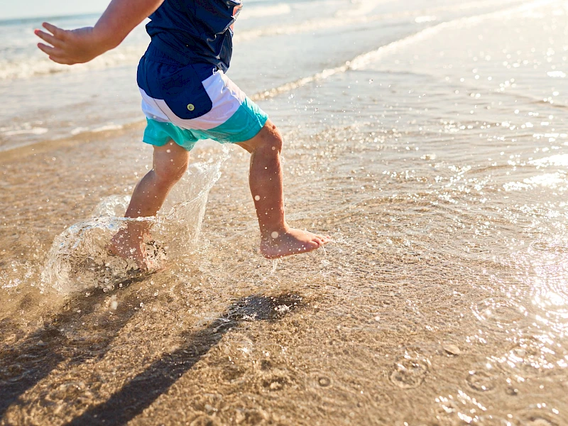 A child runs along the shore, splashing through shallow waves as water ripples with each step at the beach.