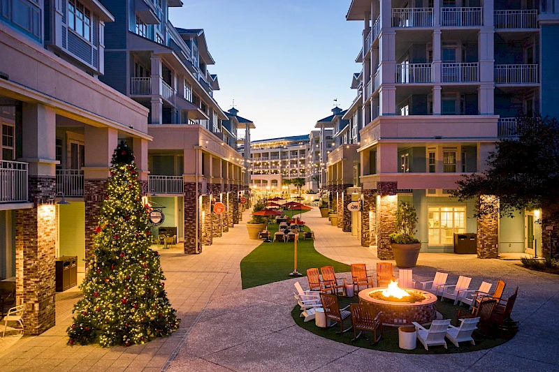 A group of friends enjoys a sunny outdoor meal by the pool, sharing food and drinks while chatting happily in smart casual attire.