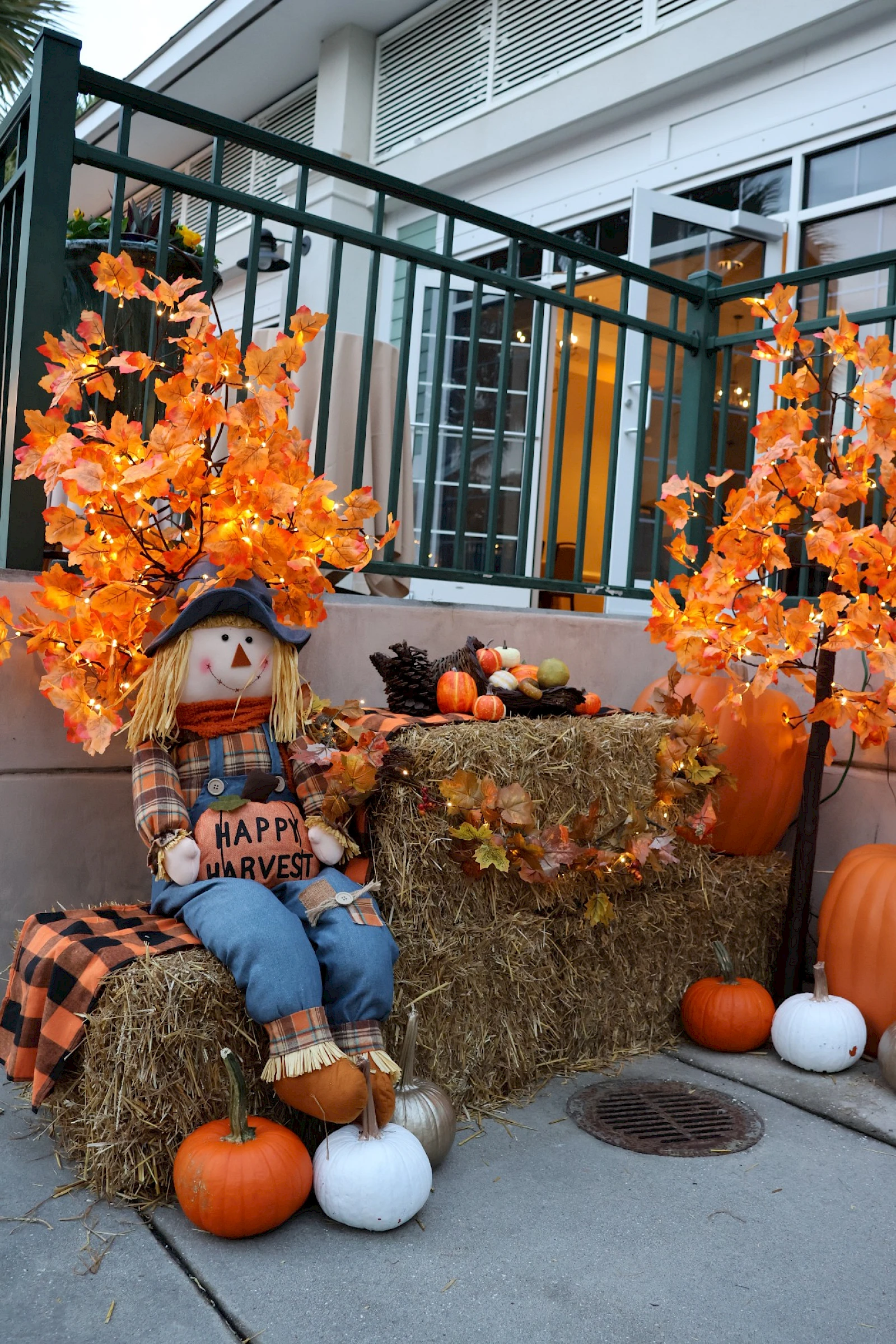 Autumn display: a scarecrow on hay bales with orange leaves, pumpkins, and seasonal decor at a porch.