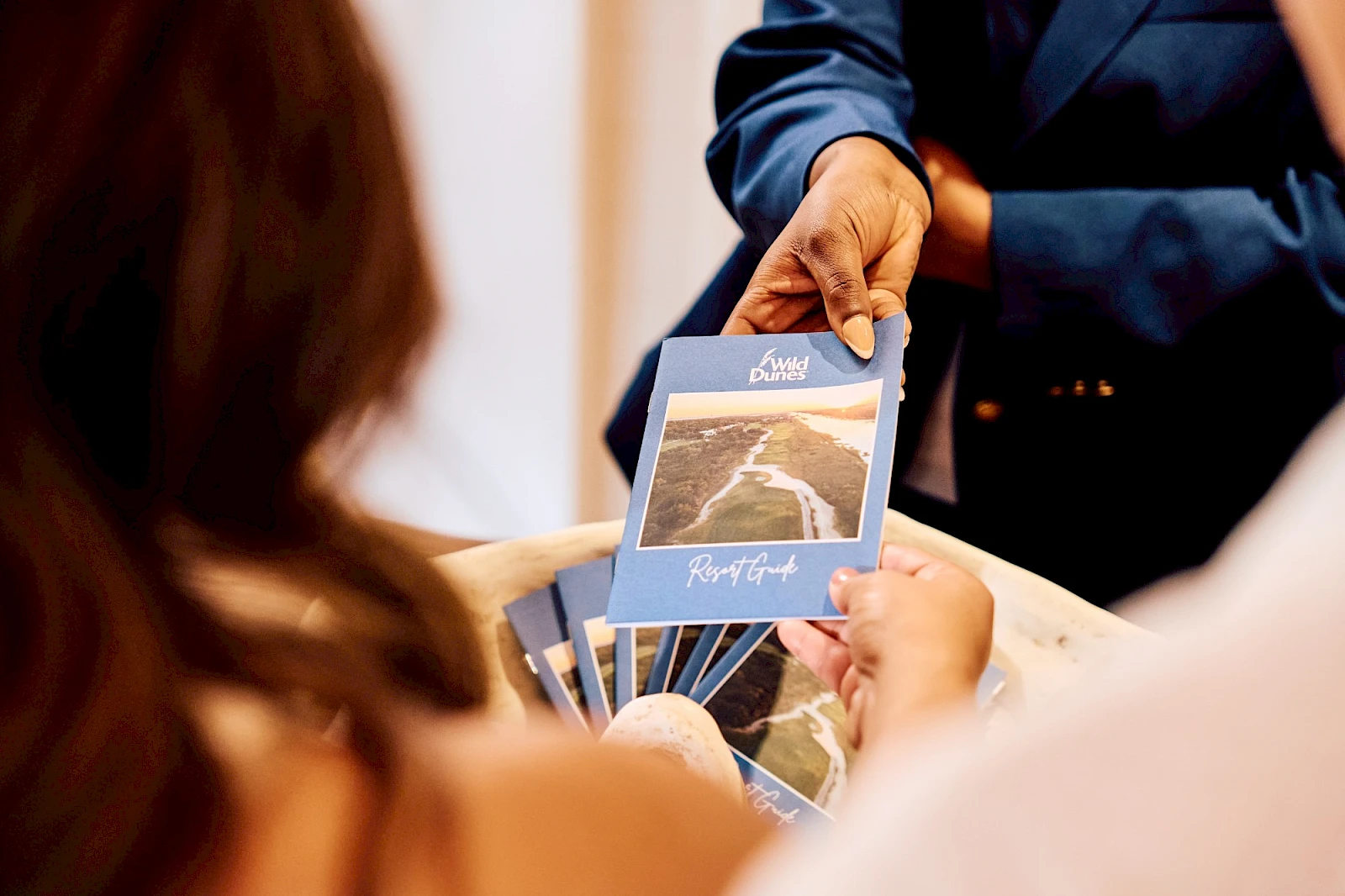 A person hands out blue-tinted cards or bookmarks with a scenic photo; others reach to grab them in a blurred setting.