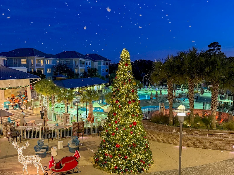 A festive outdoor scene with a tall Christmas tree, twinkling lights, a sleigh cutout, and people by a pool area under a starry night sky.