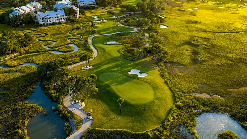 An aerial view of a lush golf course with winding water hazards, green fairways, and resort buildings in the background, nestled in nature.