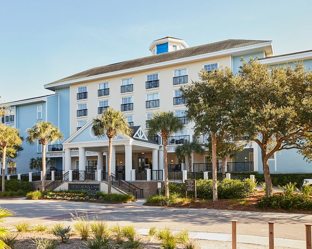 A large light-blue hotel with a white entrance, palm trees, and a drop-off area in front.