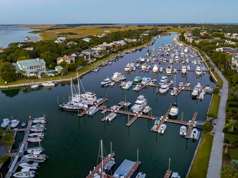 Aerial view of a marina with numerous boats and yachts docked along wooden piers, surrounded by residential buildings and waterways.