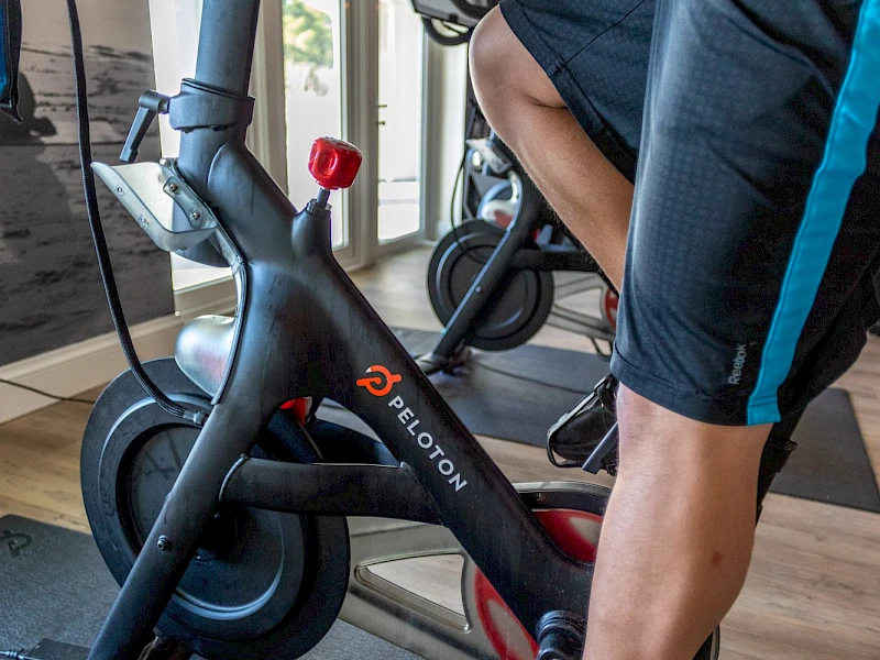 Person on a stationary bike trainer indoors, close-up of legs; bike labeled "FOIRON" with red water bottle cap nearby.