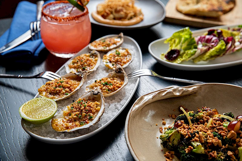 Oysters Rockefeller topped with crunchy breadcrumbs, a lime wedge, a leafy salad bowl, and a colorful spread of small plates—delicious.