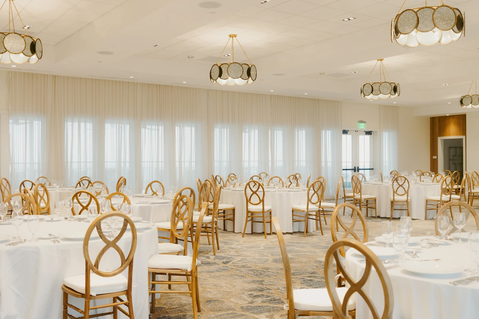 A spacious banquet hall set up for an event with round tables, white tablecloths, and wooden chairs.