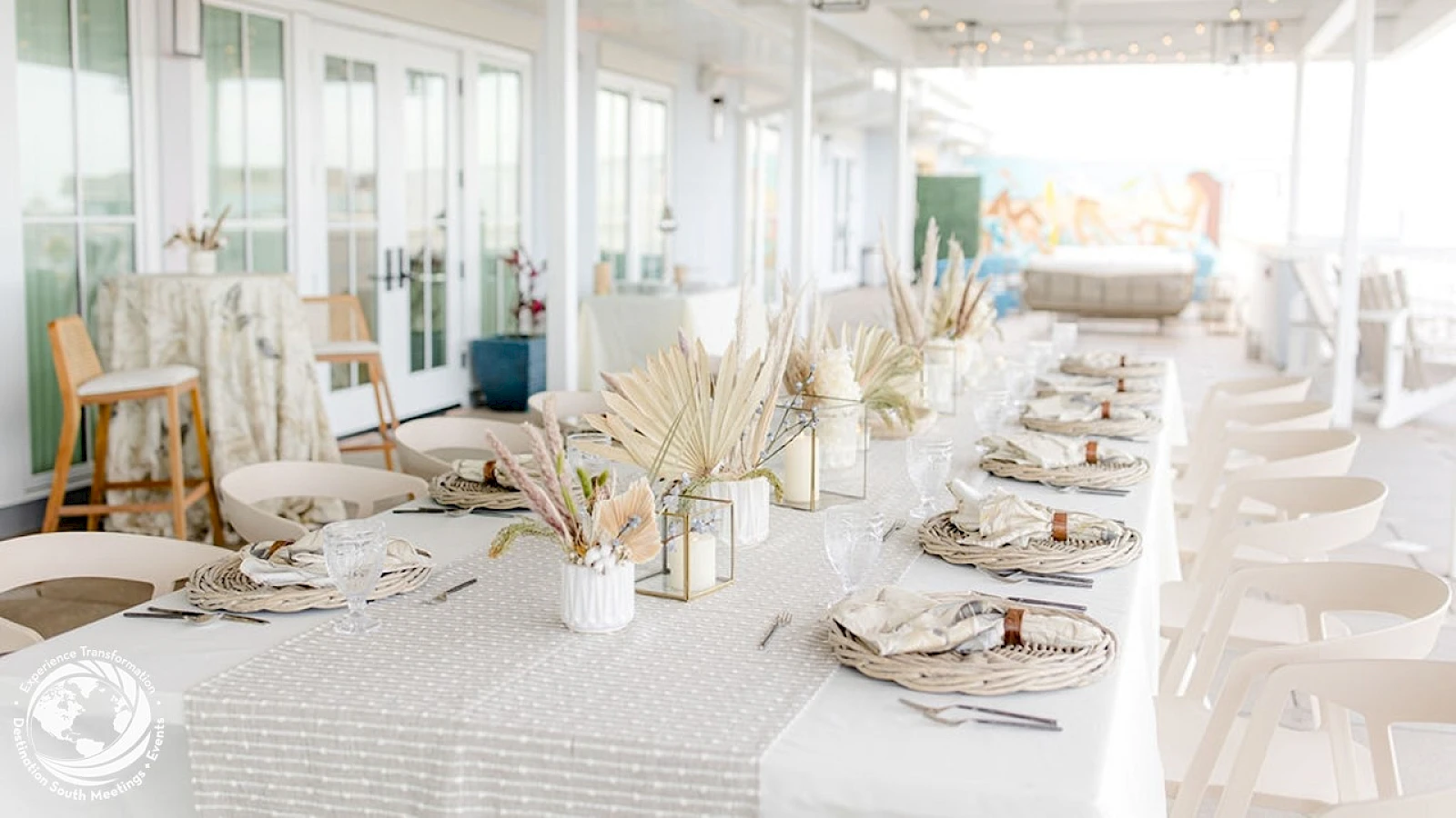 A bright coastal dining setup with a long white table, linen runners, place settings, and natural centerpiece grasses; airy and elegant.