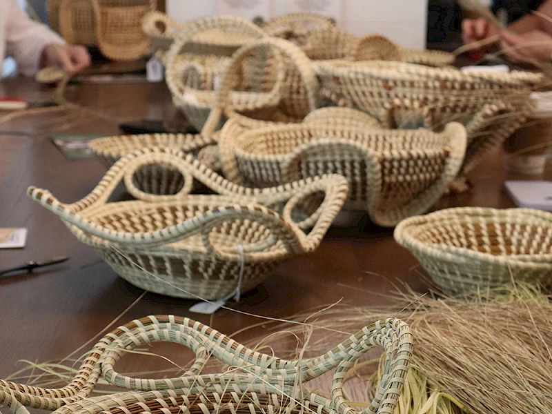 A table of woven baskets in natural tones, ready for display; baskets of various sizes with straw accents and crafting tools nearby.
