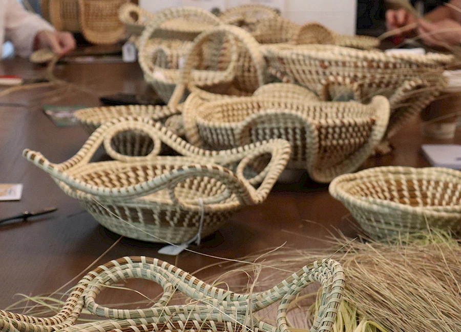 A table of woven baskets in natural tones, ready for display; baskets of various sizes with straw accents and crafting tools nearby.