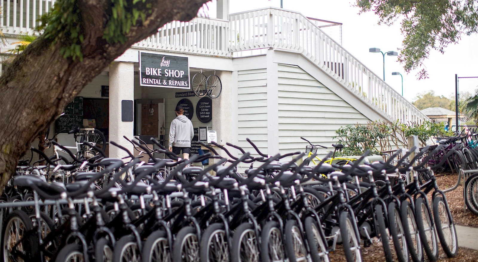 A bike shop with rental/repairs, white building, lots of parked bikes in front, and a person entering the doorway.