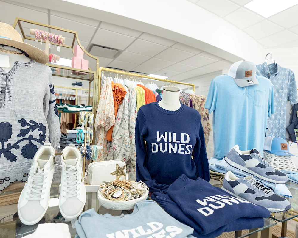 A clothing store display featuring blue “WILD DUNES” apparel and accessories, including shirts, sandals, and hats, arranged neatly.