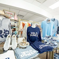 A clothing store display featuring blue “WILD DUNES” apparel and accessories, including shirts, sandals, and hats, arranged neatly.