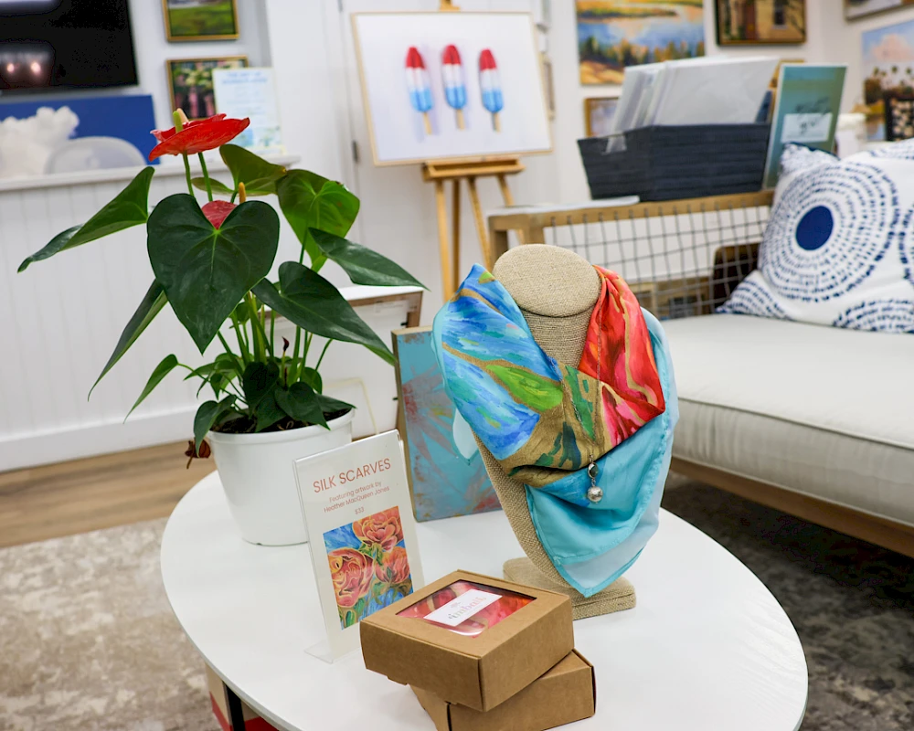 A cozy showroom with a potted plant, a mannequin bust draped in colorful fabric, and small boxes on a white coffee table in front of a couch.