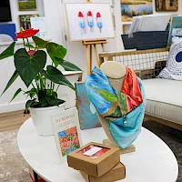 A cozy showroom with a potted plant, a mannequin bust draped in colorful fabric, and small boxes on a white coffee table in front of a couch.