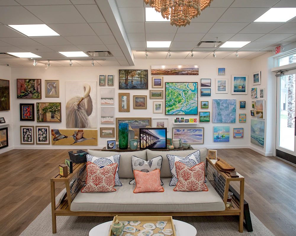 A cozy art gallery with a sofa, colorful cushions, and numerous paintings hung on white walls.