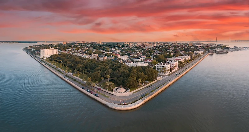 Aerial view of a triangular peninsula with a tree-lined park, surrounding water, and low-rise buildings at sunset.