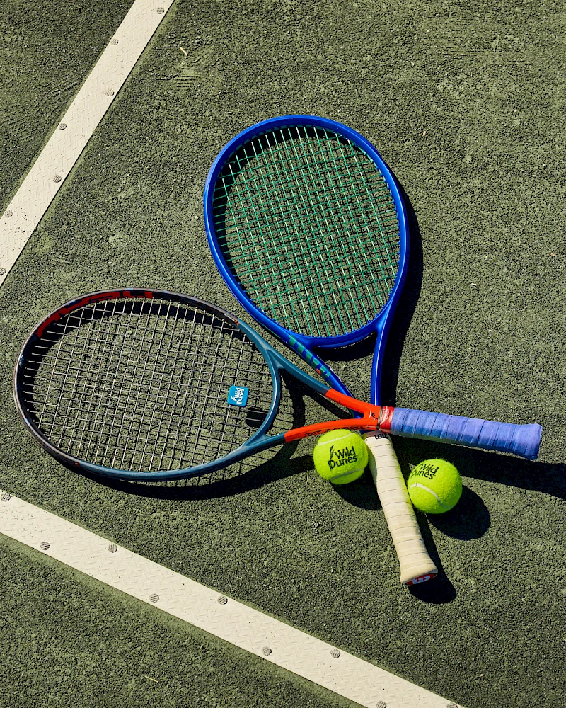 Tennis gear on a court: two rackets, three balls, and a couple of grips lying near the lines, ready for a match.