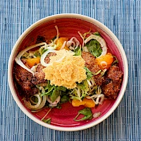 A colorful bowl of beef or meat with greens, onions, peppers, and a crispy topping on top, all on a blue placemat.