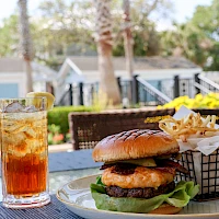 A burger with lettuce, a side of fries, and a glass of iced tea on an outdoor table, sunny day.