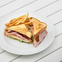 A plated ham and cheese club sandwich with crispy fries on the side, cut in half to reveal ham, cheese, lettuce, and tomato.