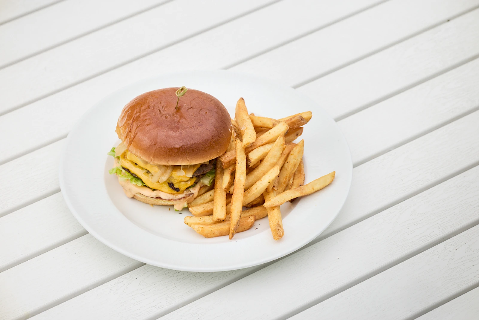 A cheeseburger with lettuce, cheese, and a beef patty on a bun, served with a generous pile of french fries on a white plate.