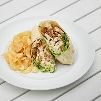 A plate with a wrap sandwich and a side of potato chips on a white table.