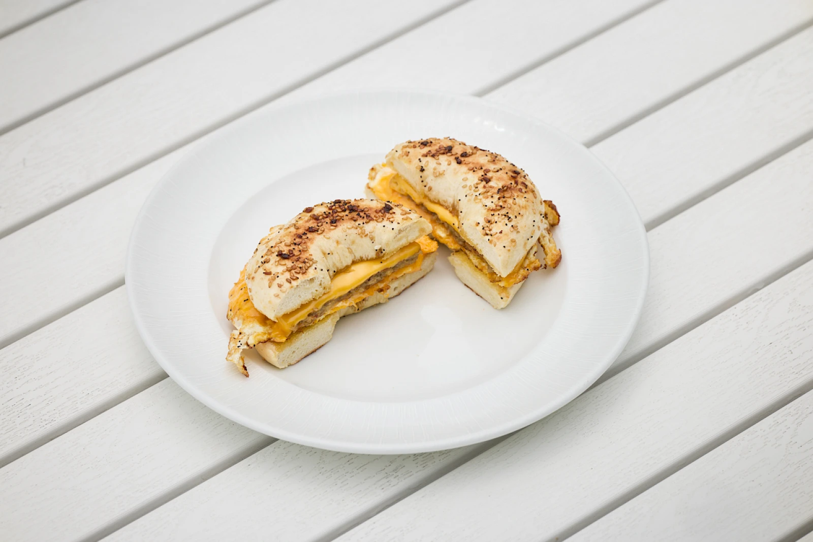 Two grilled cheese sandwiches folded in half on a white plate, cut and served on a light wooden table.