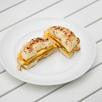Two grilled cheese sandwiches folded in half on a white plate, cut and served on a light wooden table.