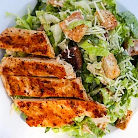 Grilled chicken strips on a crisp romaine Caesar-style salad with croutons and grated cheese, light and fresh.