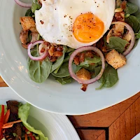 A fresh salad with baby greens, onions, croutons, bacon bits, and a sunny-side-up egg on top, with a light peppery finish.