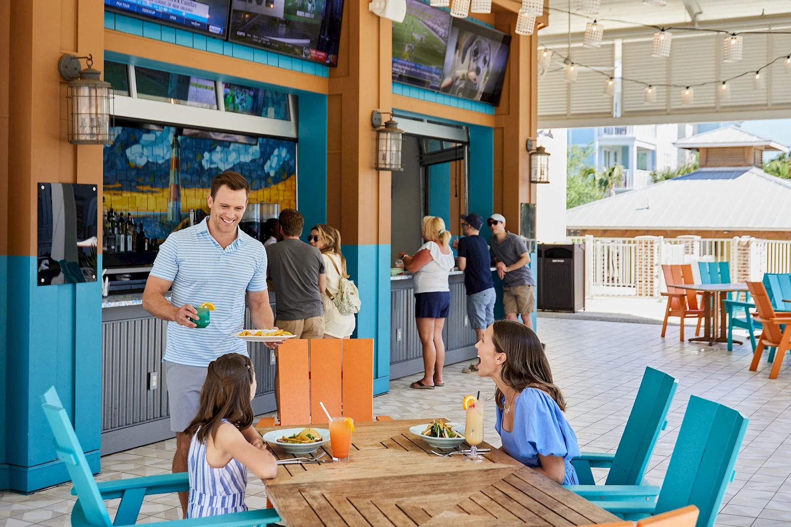 A sunny outdoor bar/restaurant with people casually dining and ordering drinks at a bright, tropical-looking venue.