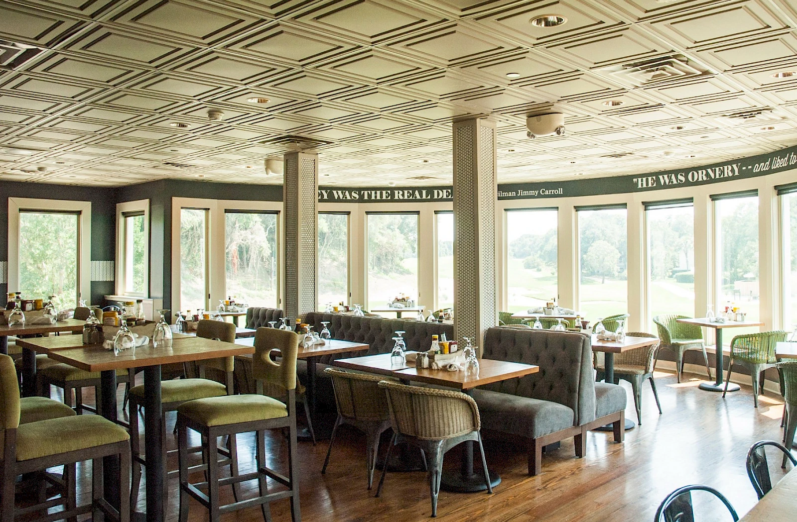 A bright, airy restaurant or cafe with large windows, wooden floors, and a mix of cushioned booths and chairs; daytime dining setup.