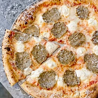 Whole pepperoni and cheese pizza, sliced, cooling on a rustic surface, with a golden crust and bubbling mozzarella.