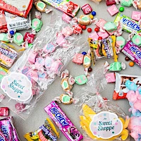 A colorful mess of assorted candies and lollipops scattered on a surface, in wrappers and pink cotton candy clusters. ending the sentence.