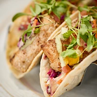 Two soft tacos filled with colorful veggies, crispy tofu or chicken, and fresh microgreens on a plate, vibrant and appetizing.