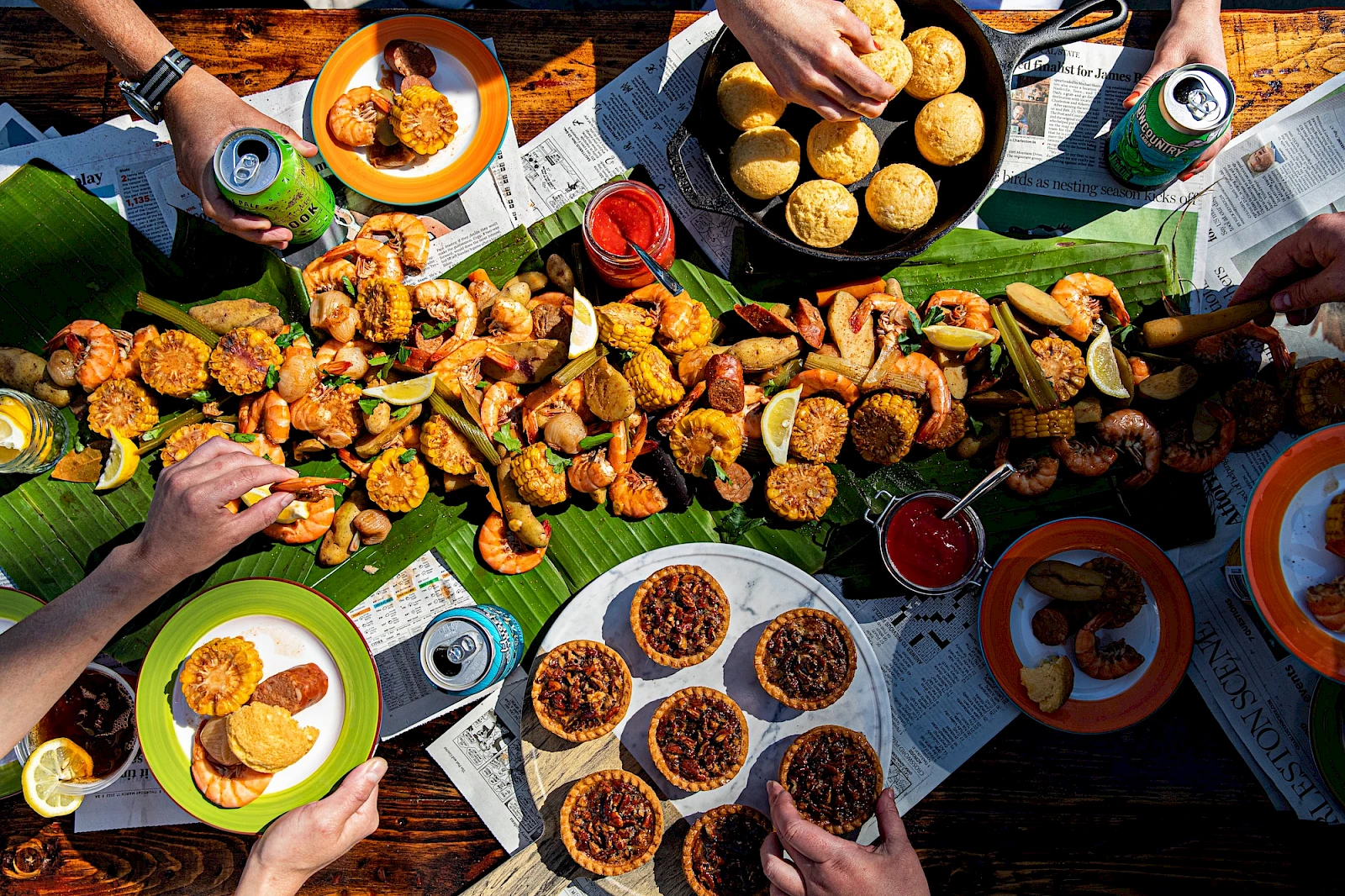 A colorful outdoor feast of fried chicken bites, sliders, assorted dips, deviled eggs, mini tarts, cookies, and drinks laid out on a table.