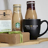 A coffee gift set: bag of beans, two bottles (milk/creamer), a mug reading “King Bean Coffee Roasters,” and a wrapped treat on a wooden tray.