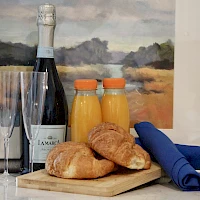 A classy breakfast setup with sparkling wine, orange juice, two croissants, and blue napkins on a wooden board.