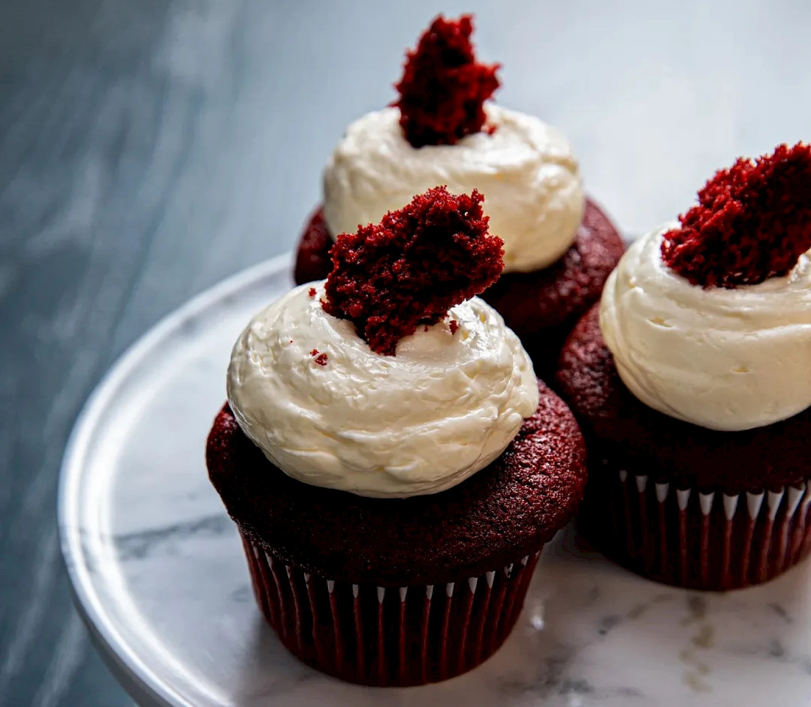 Red velvet cupcakes topped with white frosting and a red cake crumble garnish on a silver plate.
