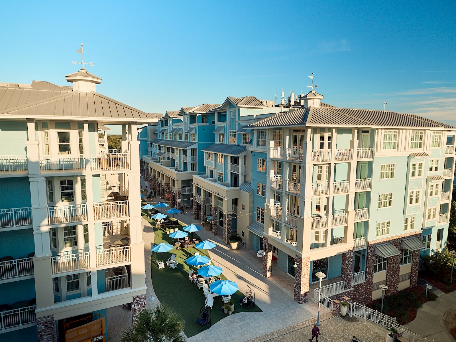 Cozy beachfront condo complex with pastel blue buildings, a central courtyard, and a row of blue umbrellas over outdoor tables.
