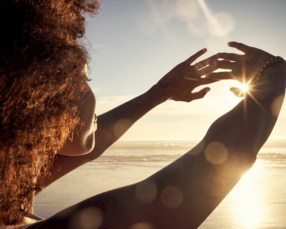 Two people at the beach sharing a sunlit moment, reaching toward the horizon as the sun shines between them.