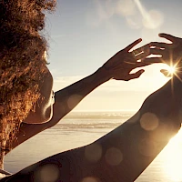 Two people at the beach sharing a sunlit moment, reaching toward the horizon as the sun shines between them.