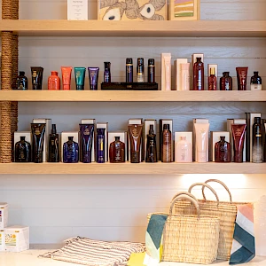 Shelves with grooming products and bags on a counter; various bottles, boxed items, and a woven tote bag with a striped cloth nearby.