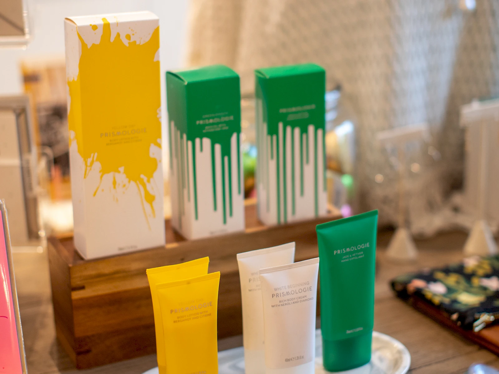 A display of colorful tubes and boxes with paint-like drips in yellow, green, and white, arranged on a wooden stand in a boutique setting.