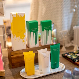 A display of colorful tubes and boxes with paint-like drips in yellow, green, and white, arranged on a wooden stand in a boutique setting.