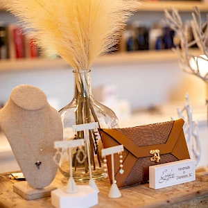 A cozy craft setup on a wooden table with dried bouquet, white display stands, and a small brown box, nicely arranged against a blurred shop backdrop.